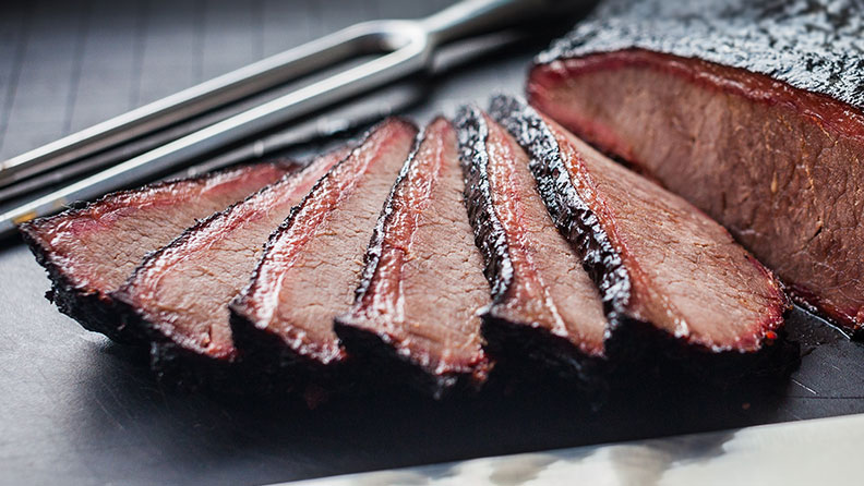 a brisket cut into pieces with knife in the background